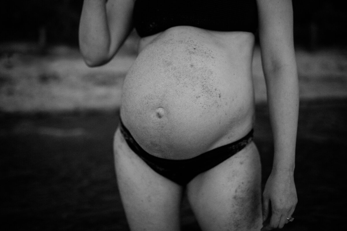 Black and white photo of pregnant woman wearing bikini at Melbourne beach, sand on skin.