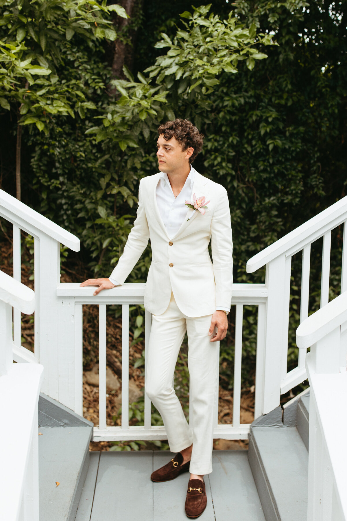 Groom in a chic white suit standing on a porch, looking off into the distance