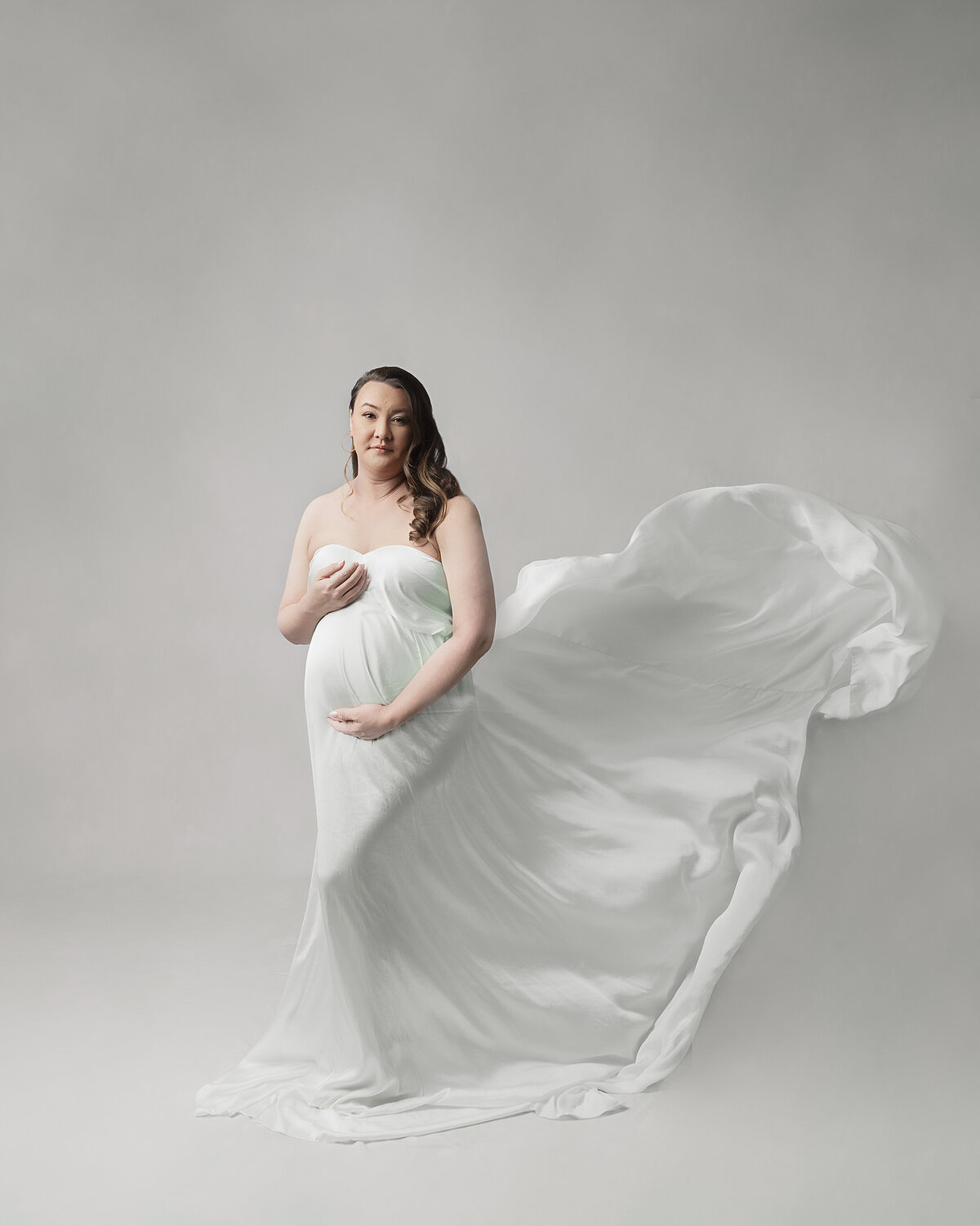 Mother pregnant with twin wearing white dress on white backdrop