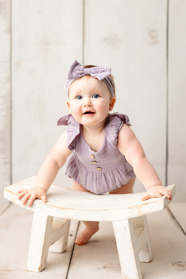 Baby girl stands with stool for her photo session.