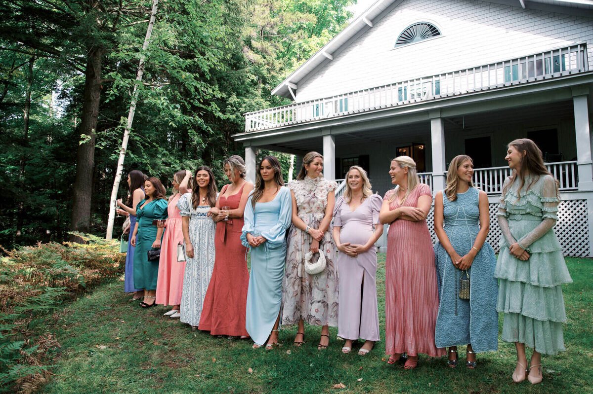 The bridesmaids are lined up outdoors with a lot of trees at The Ausable Club, New York.