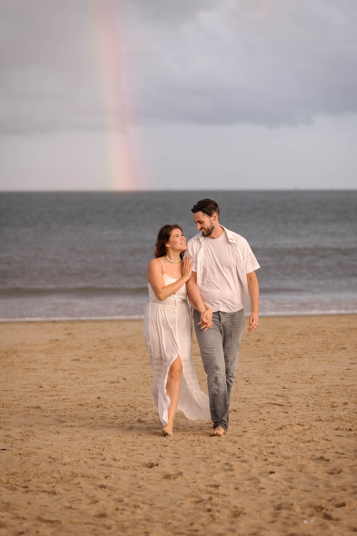 A couple walking together arm in arm on the beach on Dorset with a rainbow behind them