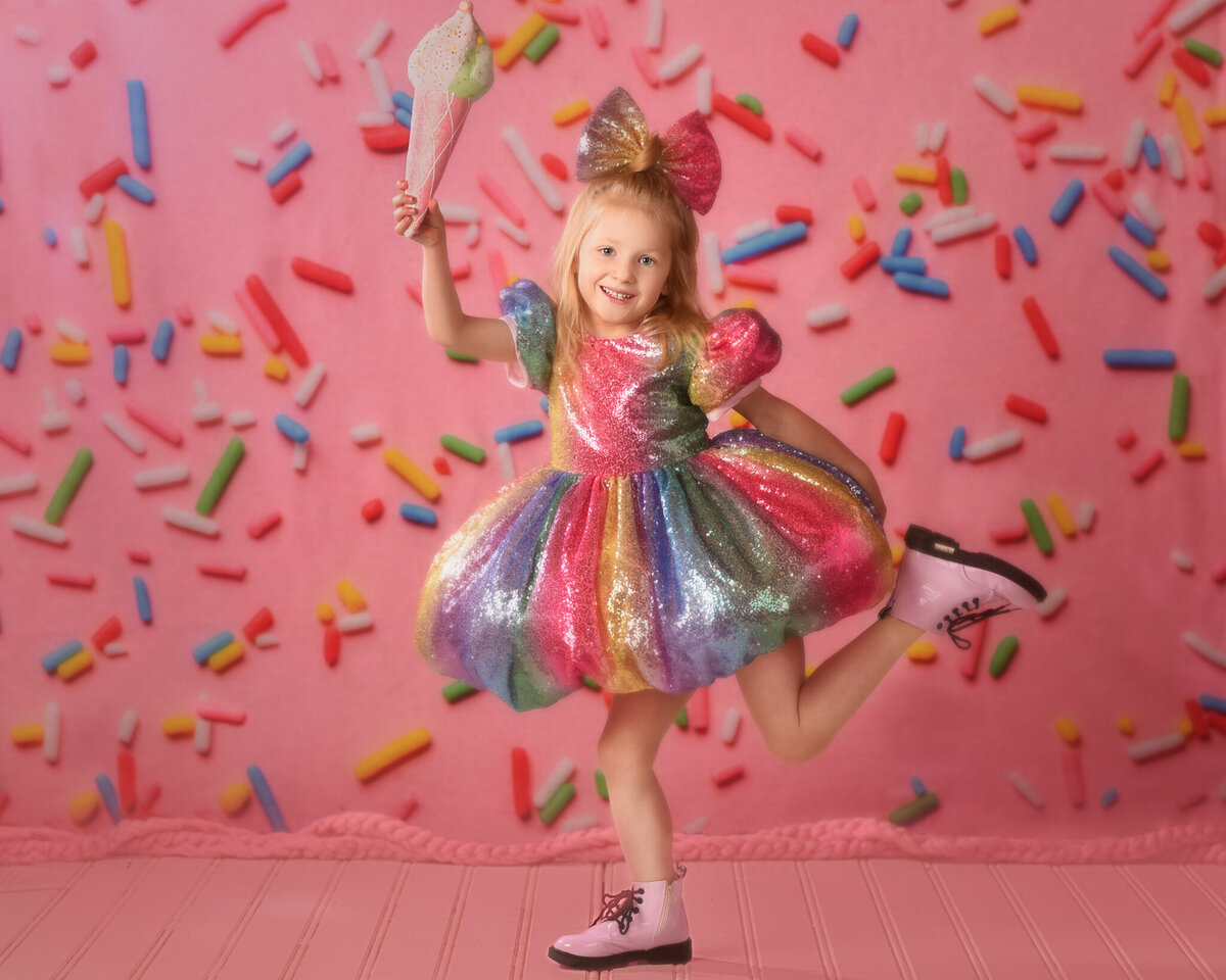 Playful portrait of a young girl in a colorful dress, surrounded by falling sprinkles against a vibrant pink backdrop. Captured in Overland Park, Kansas, this whimsical setup is ideal for families seeking joyful and imaginative child photography.