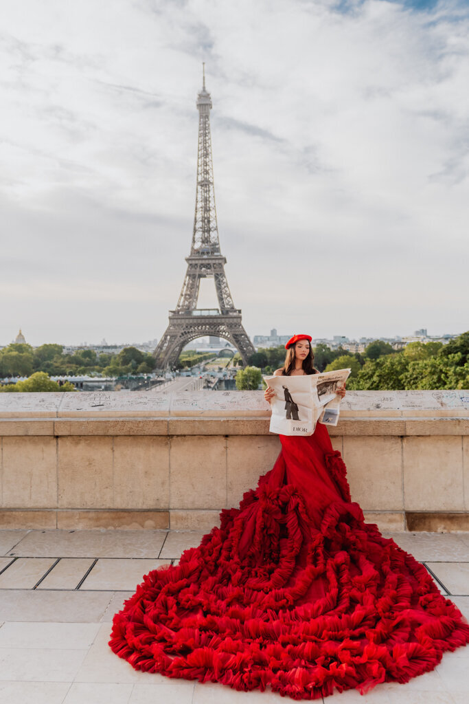Lifestyle Paris portrait with brunette reading newspaper in red princess dress and matching beret before Eiffel Tower