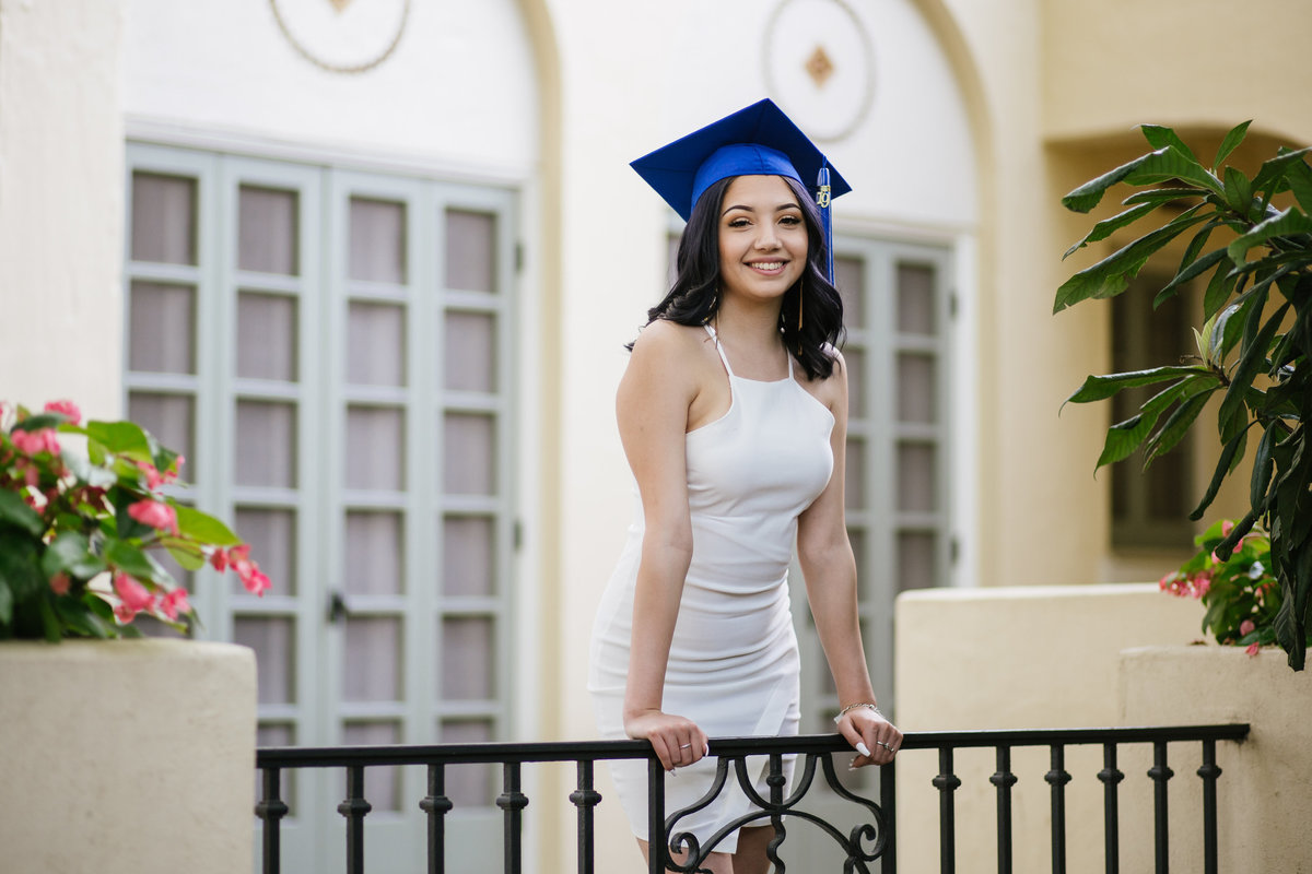 girl leaning on rail in cap and dress by San Antonio high school senior photographer