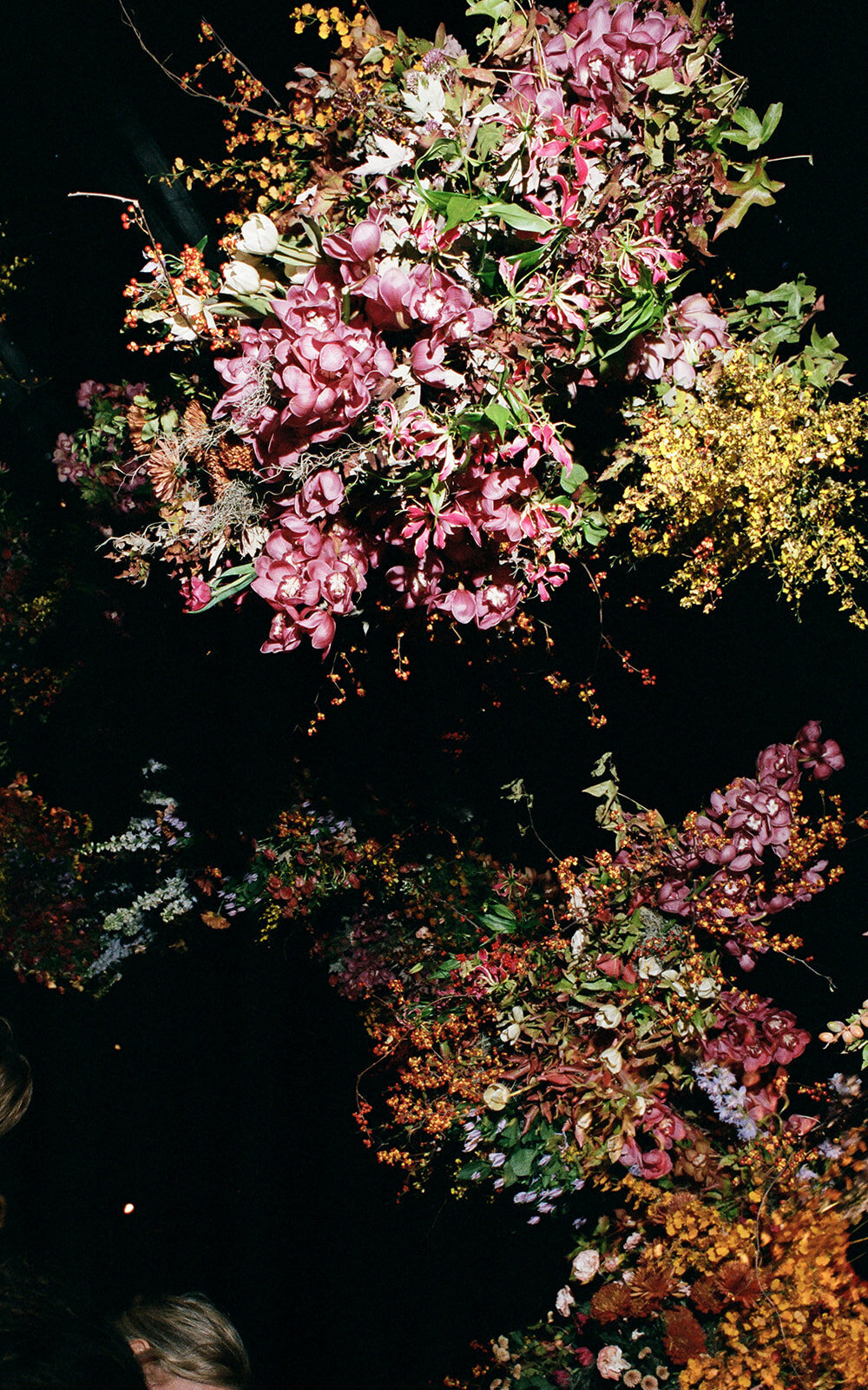 Interacting and sculptural floral clouds hang over the dance floor and bars of this fall wedding reception in Tennessee. Clear top tent build out for fall wedding reception in Tennessee hills.  Product clustered floral clouds in a tasteful fall color palette of copper, ruby, gold, burgundy, rust, and lavender. Orchids, bittersweet berries, butterfly ranunculus, and tulips are highlighted. Unique floral design with flower forward large scale installations. Design by Rosemary & Finch Floral Design in Nashville, TN.