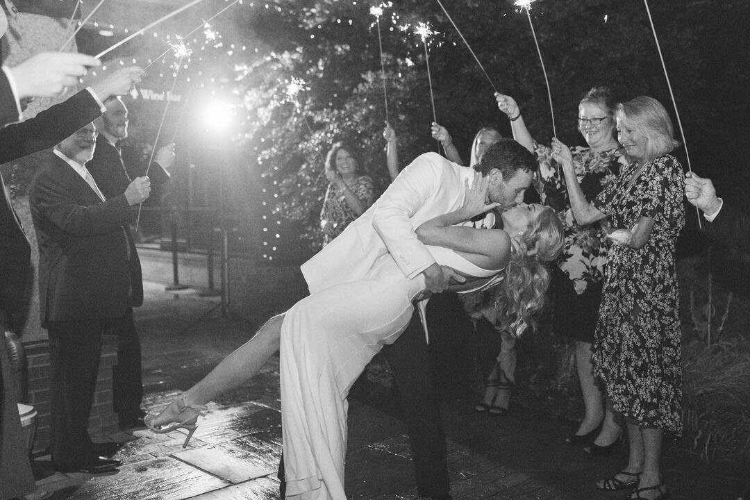 Black and White of Bride and Groom Kissing at Sparkler Exit