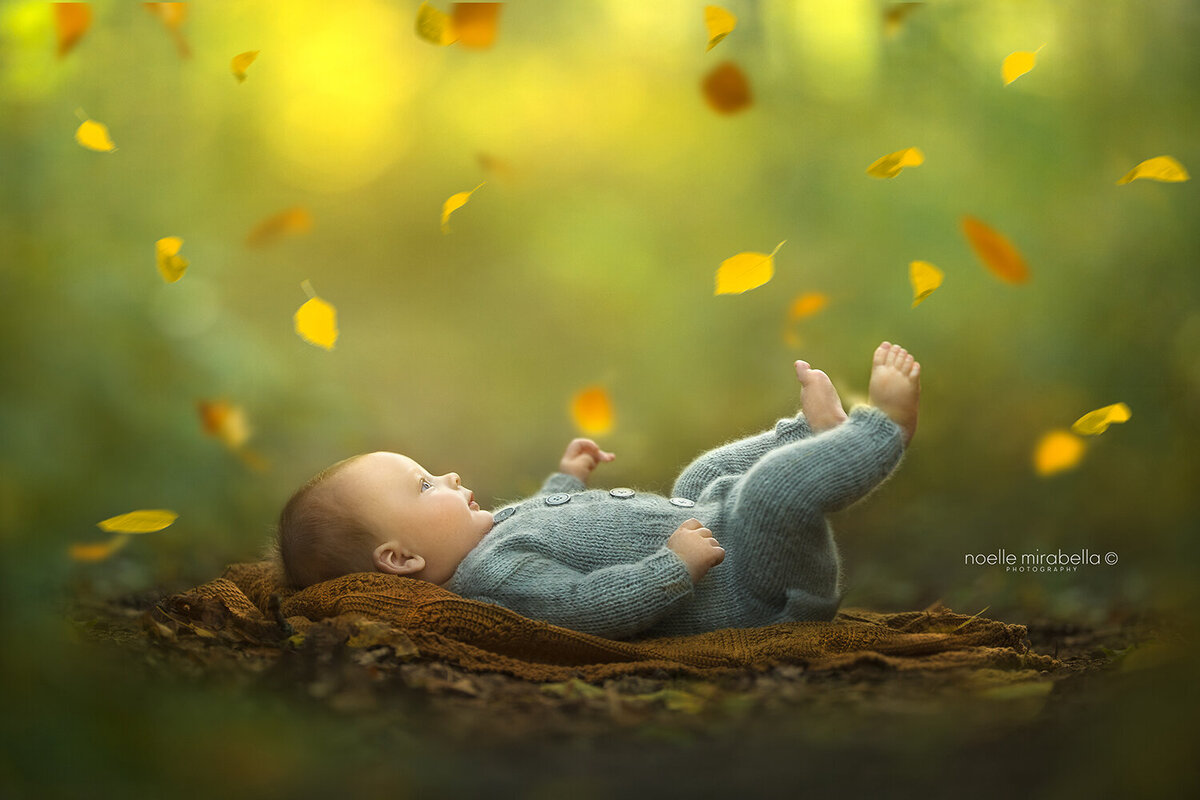 Baby laying outside on the ground with falling autumn leaves.