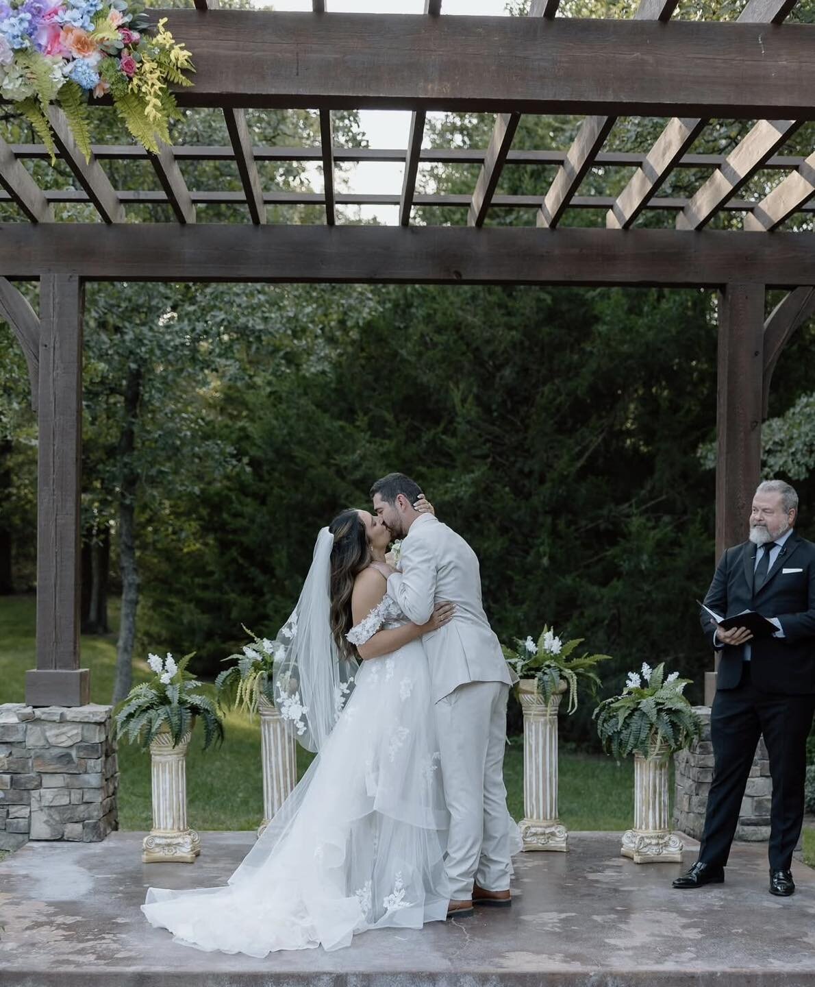 Bride and groom sharing a kiss under an outdoor pergola during their wedding ceremony