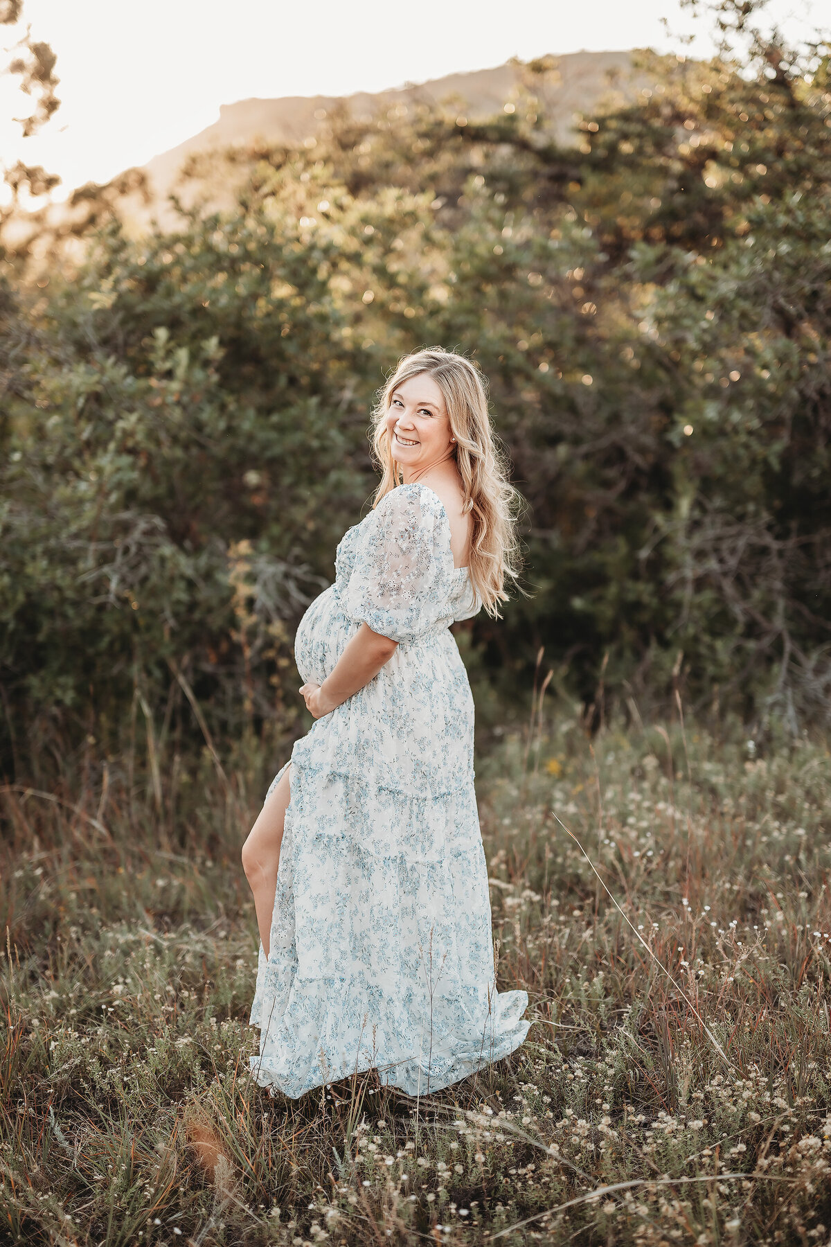 maternity woman standing sideways holding her belly and looking at maternity photographer