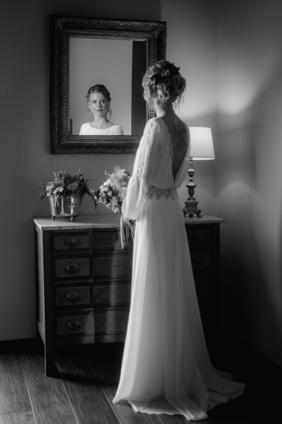 Ready for her big day, the bride stands in front of a mirror looking at it.