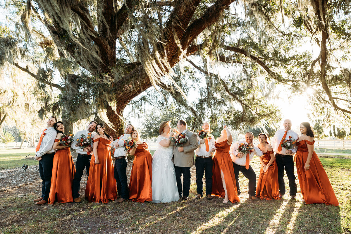 Full wedding party laughing under the sprawling moss-covered oak trees at Plantation Oaks in Callahan, Florida.