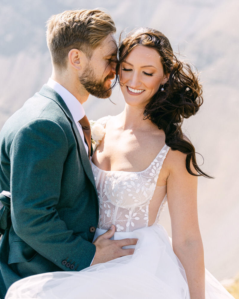This playful photograph captures the groom joking with the bride as she smiles and laughs during their portrait session in a helicopter mountain adventure wedding. The joy and connection between them shine through, making for a heartwarming and candid moment in the stunning mountain setting.