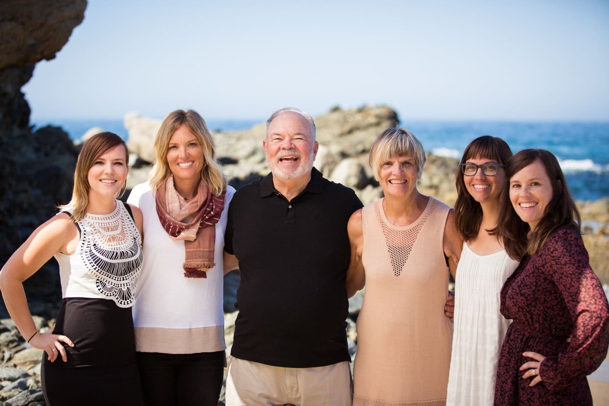 Parents pose for family photos with their four daughters with the Pacific Ocean behind them