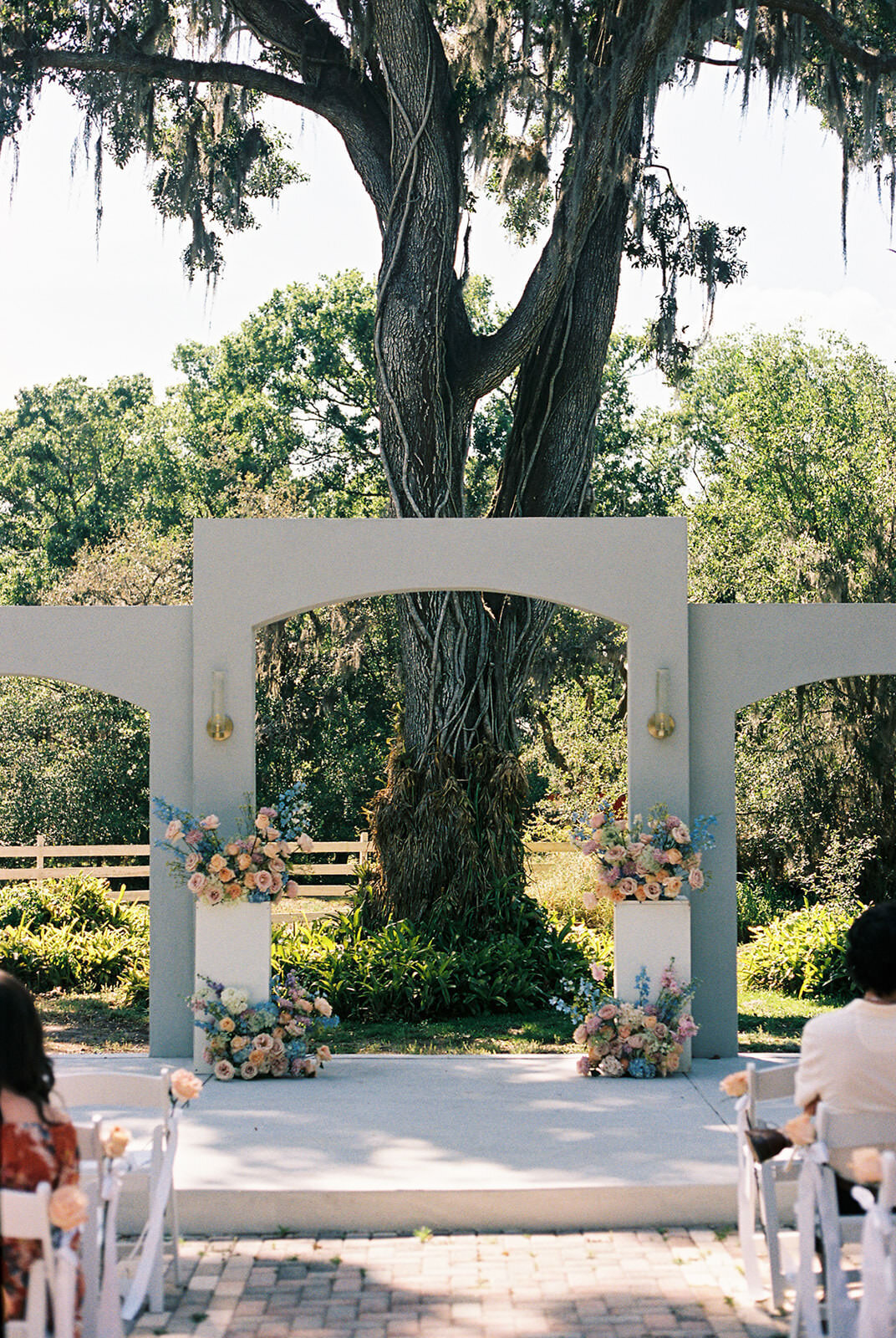 Outdoor ceremony setup with white chairs and florals on three rounded white arches at Uliana Estate in Lakeland Florida.