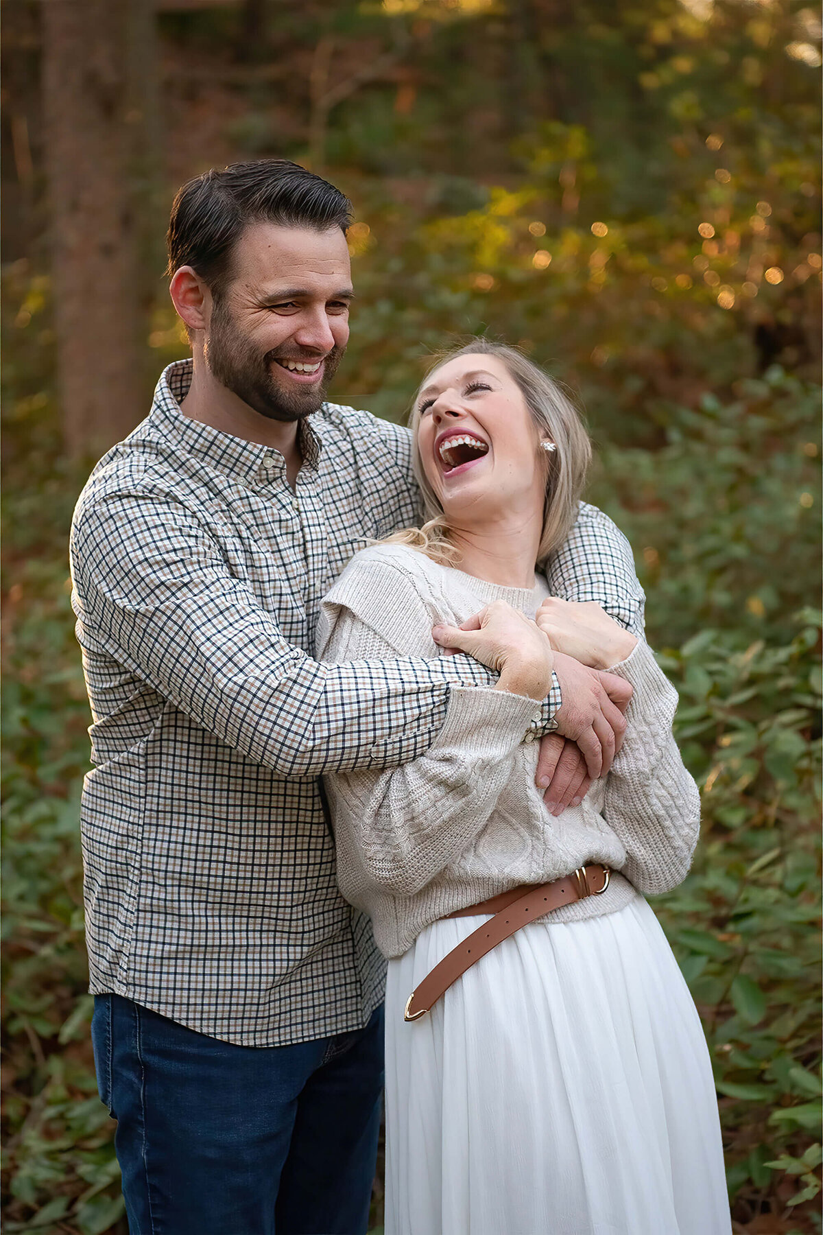 A husband has his arms around his wife while she looks up and laughs at Whip Hill park.