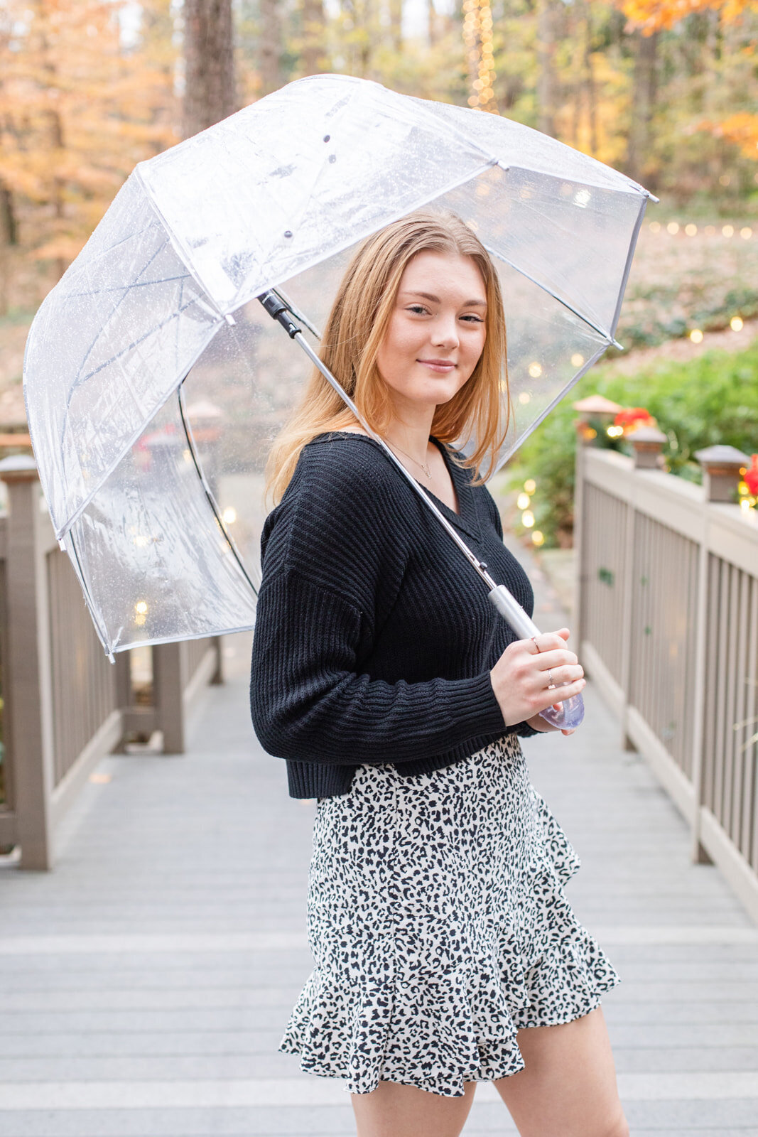 winter and rainy high school senior girl standing on a bridge and hilding a transparent umbrella in Atlanta by Laure Photography