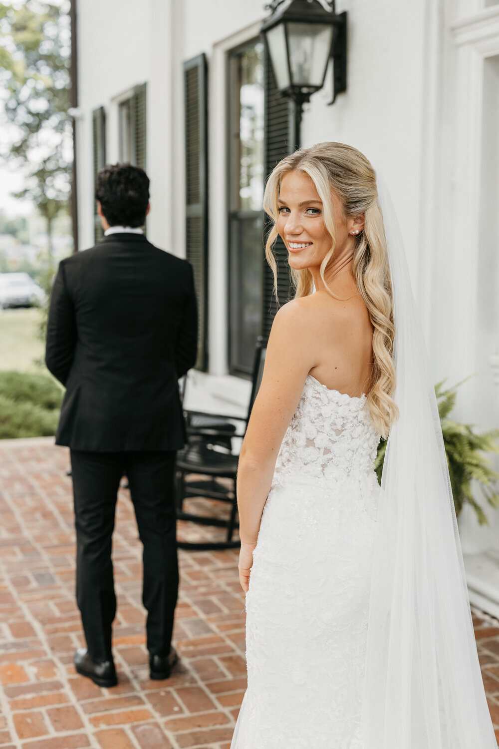 Elegant first look moment at Ashford Acres Inn, Cynthiana, KY - Bride in classic white gown approaches groom with his back turned, both standing in front of the historic venue.