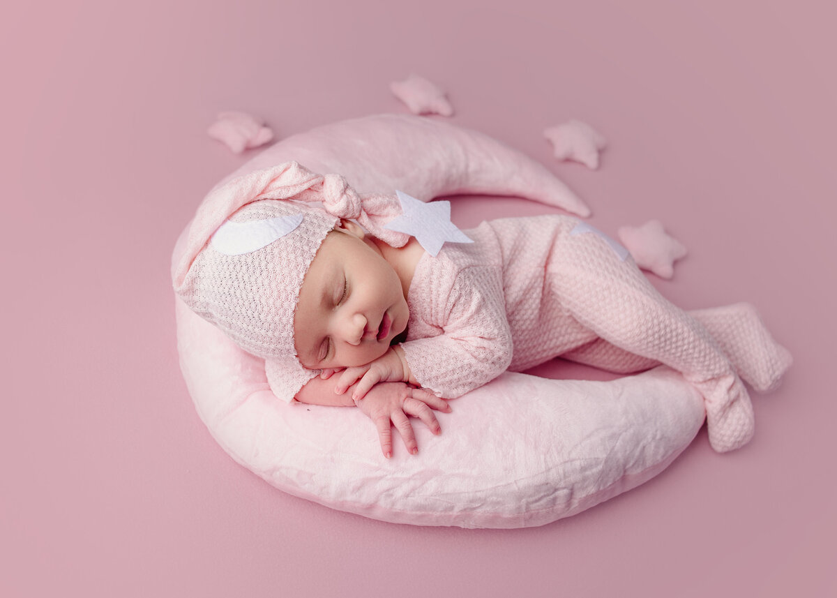 Newborn baby girl wearing pink hat laying on moon poser during newborn photoshoot in Mount Juliet tennessee photography studio