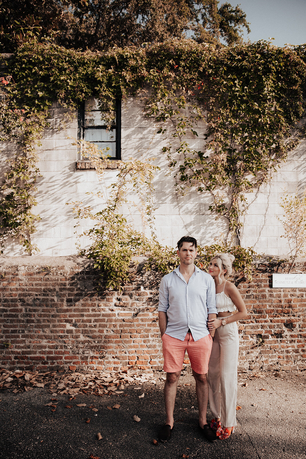 Couple standing hip to belly button in front of partly exposed brick and ivy twine