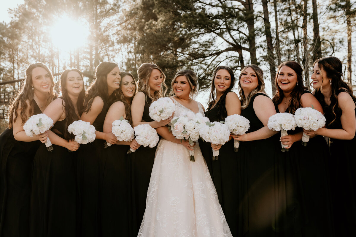 Little Rock wedding photographer photographs bride standing with her bridesmaids outside as the sunsets through the woods behind them