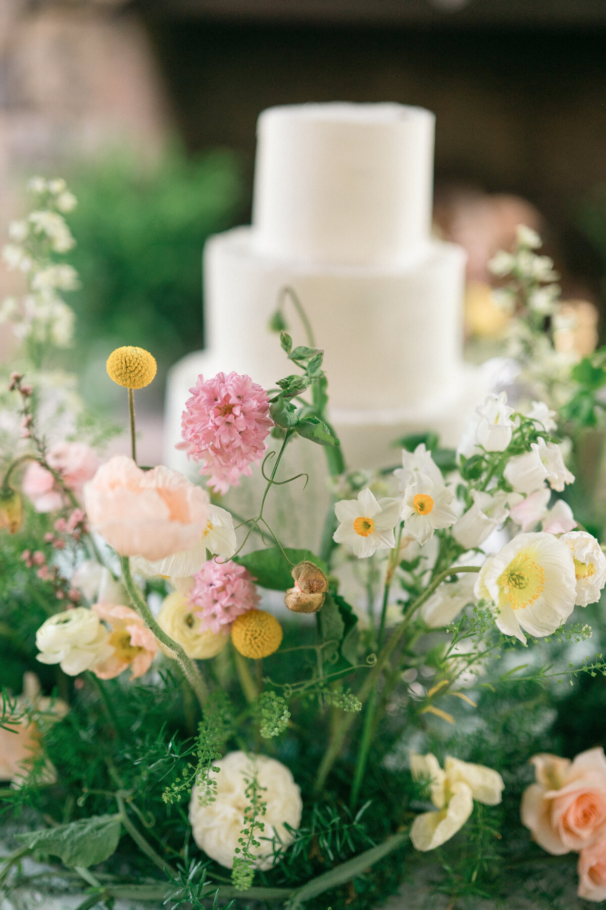 White tiered cake with flowers and greenery coming out of bottom of it