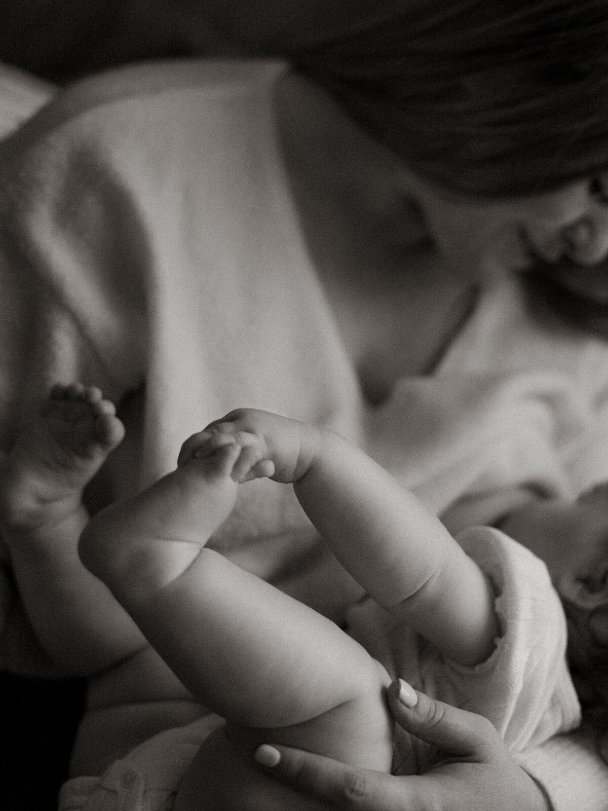 Mother in a cozy sweater breastfeeding her baby while baby holds her tiny feet.

