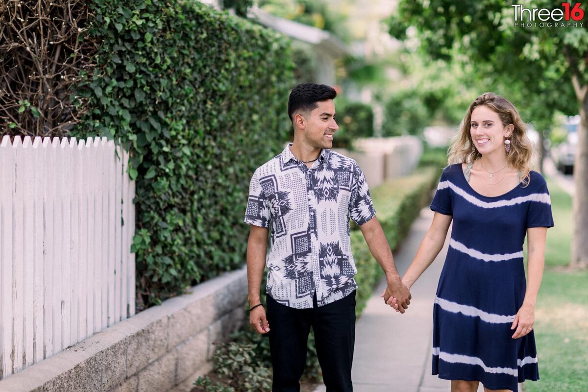 Engaged couple walk along a Downtown Brea neighborhood holding hands