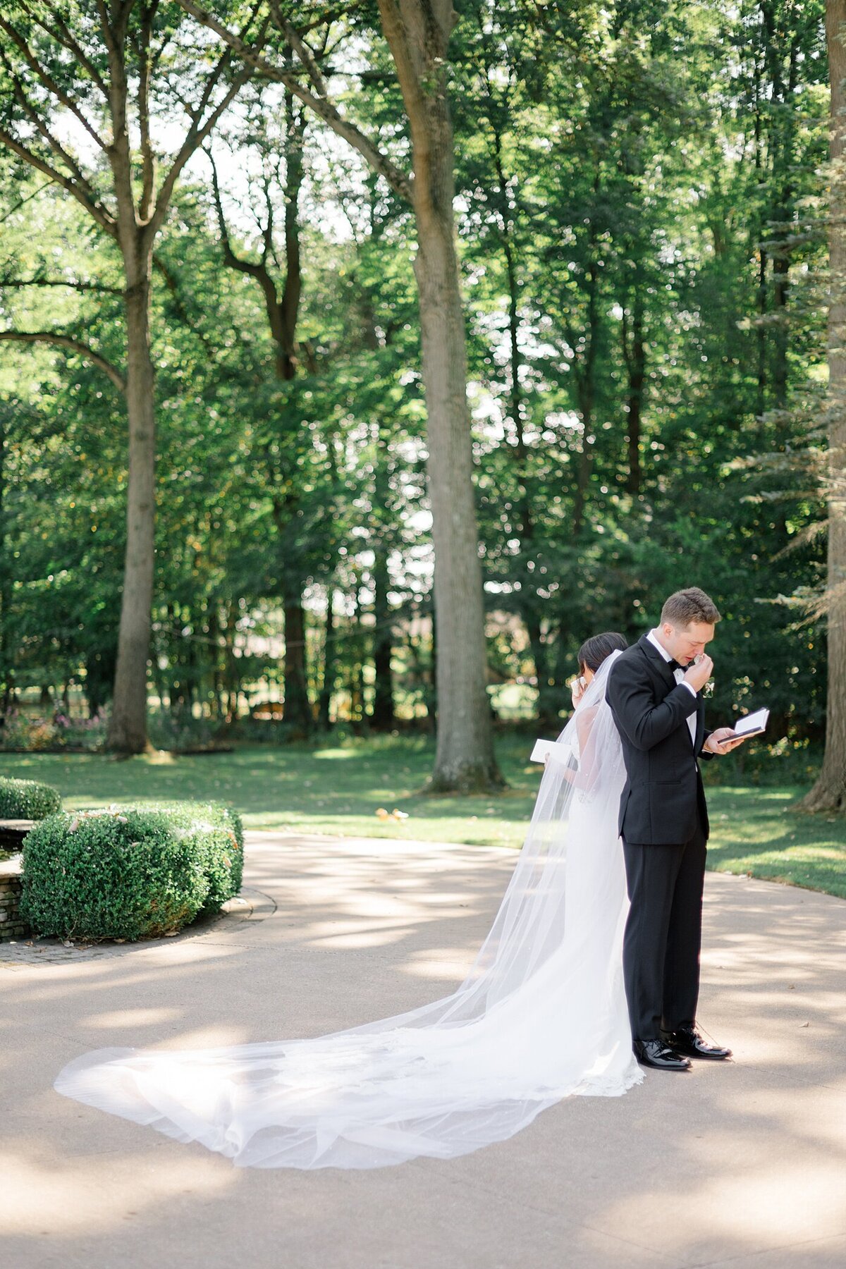 bride and groom stand back to back on a drive way while they read their private vows to one another before their wedding ceremony captured by Columbus wedding  photographer
