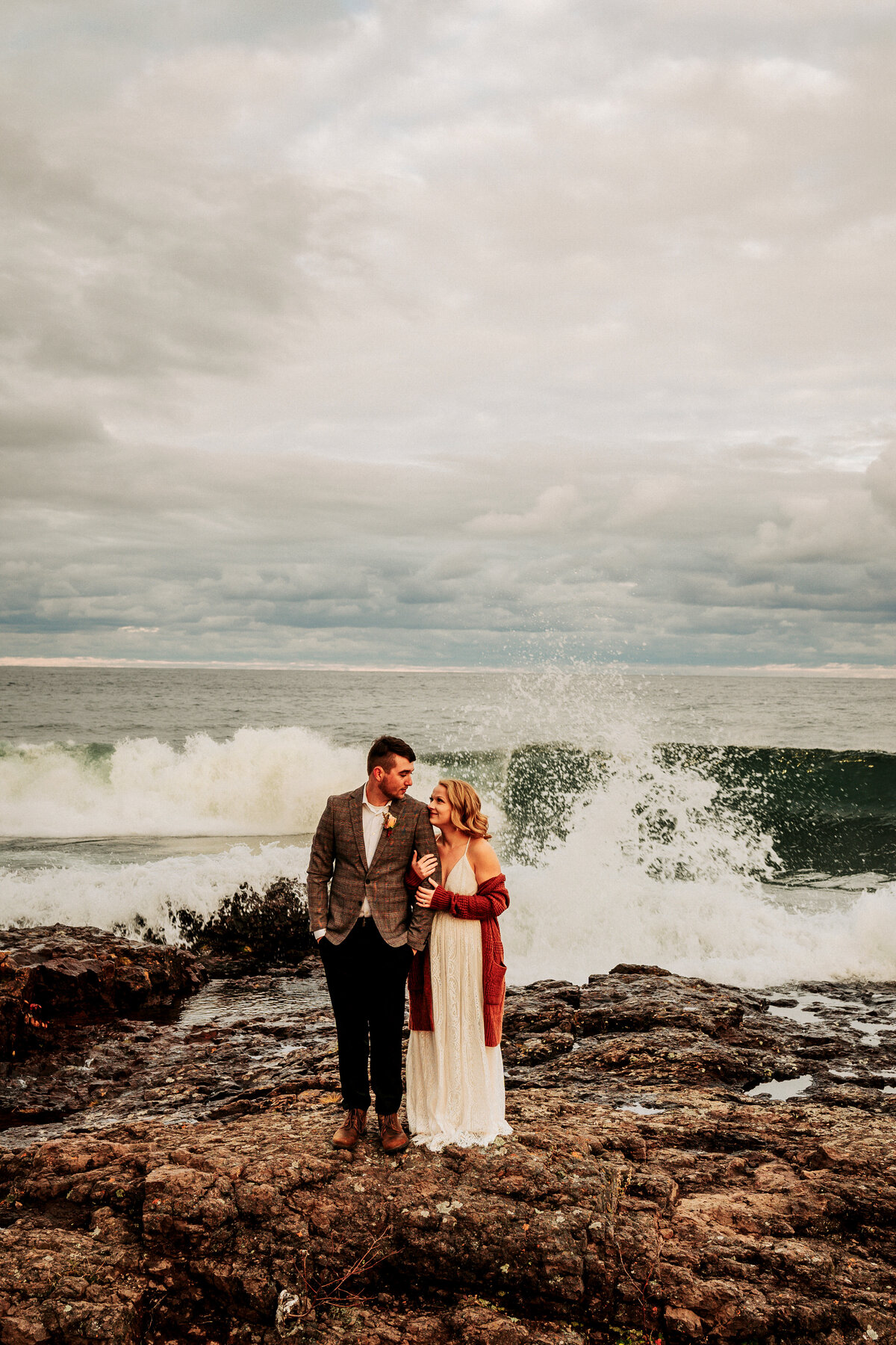 couple in front of Lake Superior with waves crashing behind them