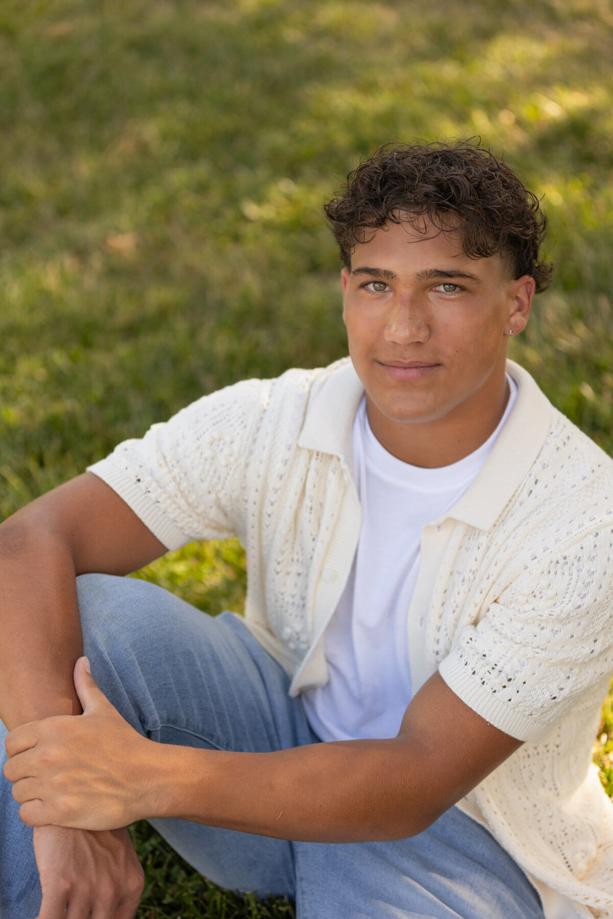 A senior guy sitting on grass looking up at the camera in Lawrence, KS