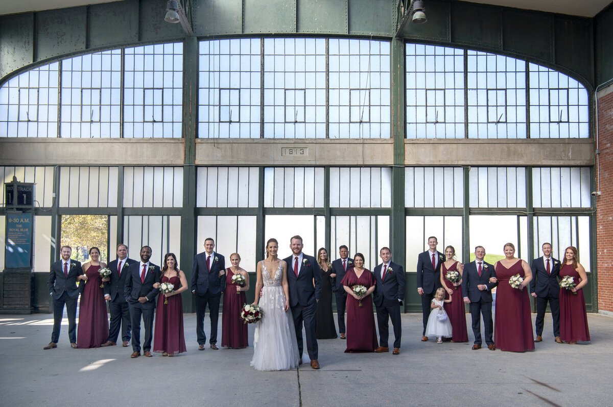 Newlyweds standing in an industrial building with their wedding parties behind them 