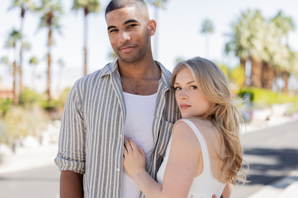 Couple walking with arms around each other, mid-stride, sharing a playful and stylish desert moment.