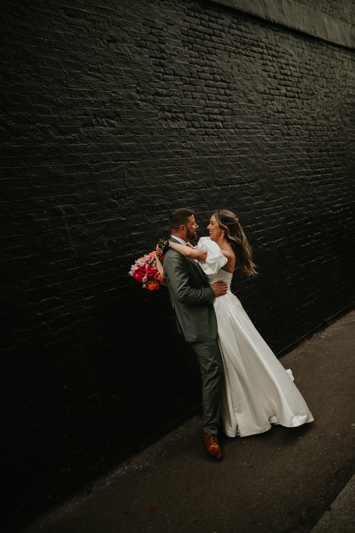 A bride wraps her arms around her groom in front of a black wall in Shoreditch. 