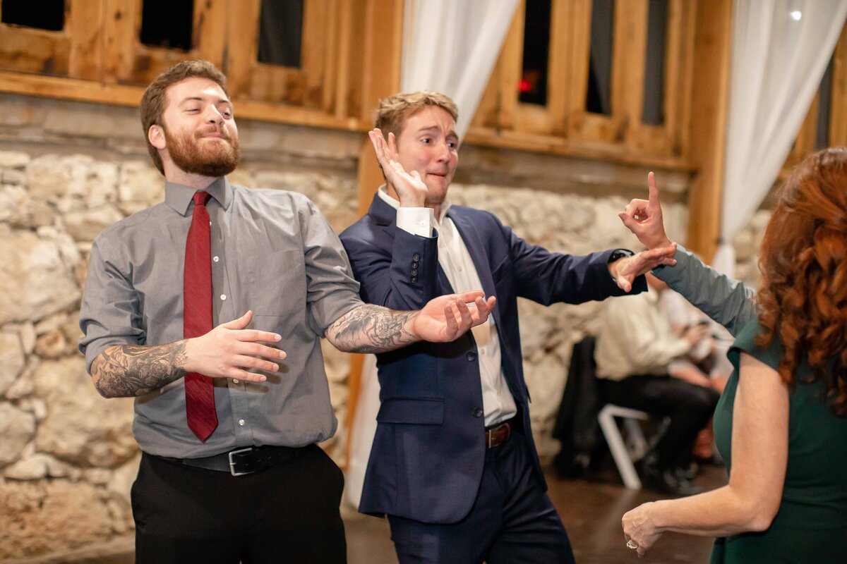 Fort Worth wedding photographer captures two male guests dancing at reception with rock wall