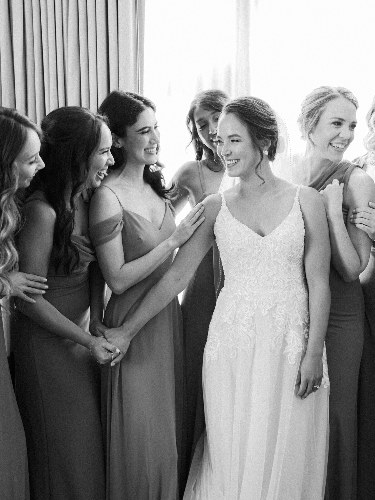 A bride holds the hand of her maid of honor while the rest of her bridesmaids huddle around her