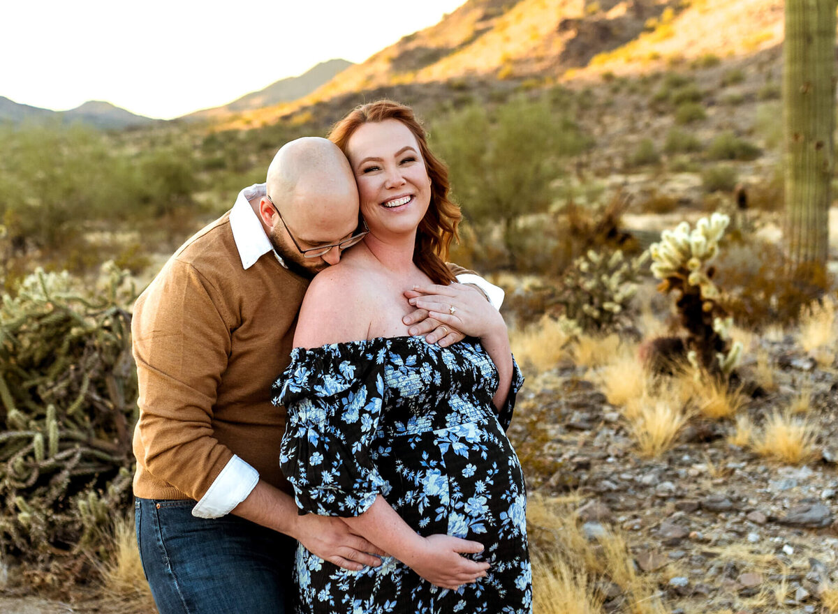tender moment for Arizona parents-to-be of husband kissing wife's shoulder and cradling baby bump