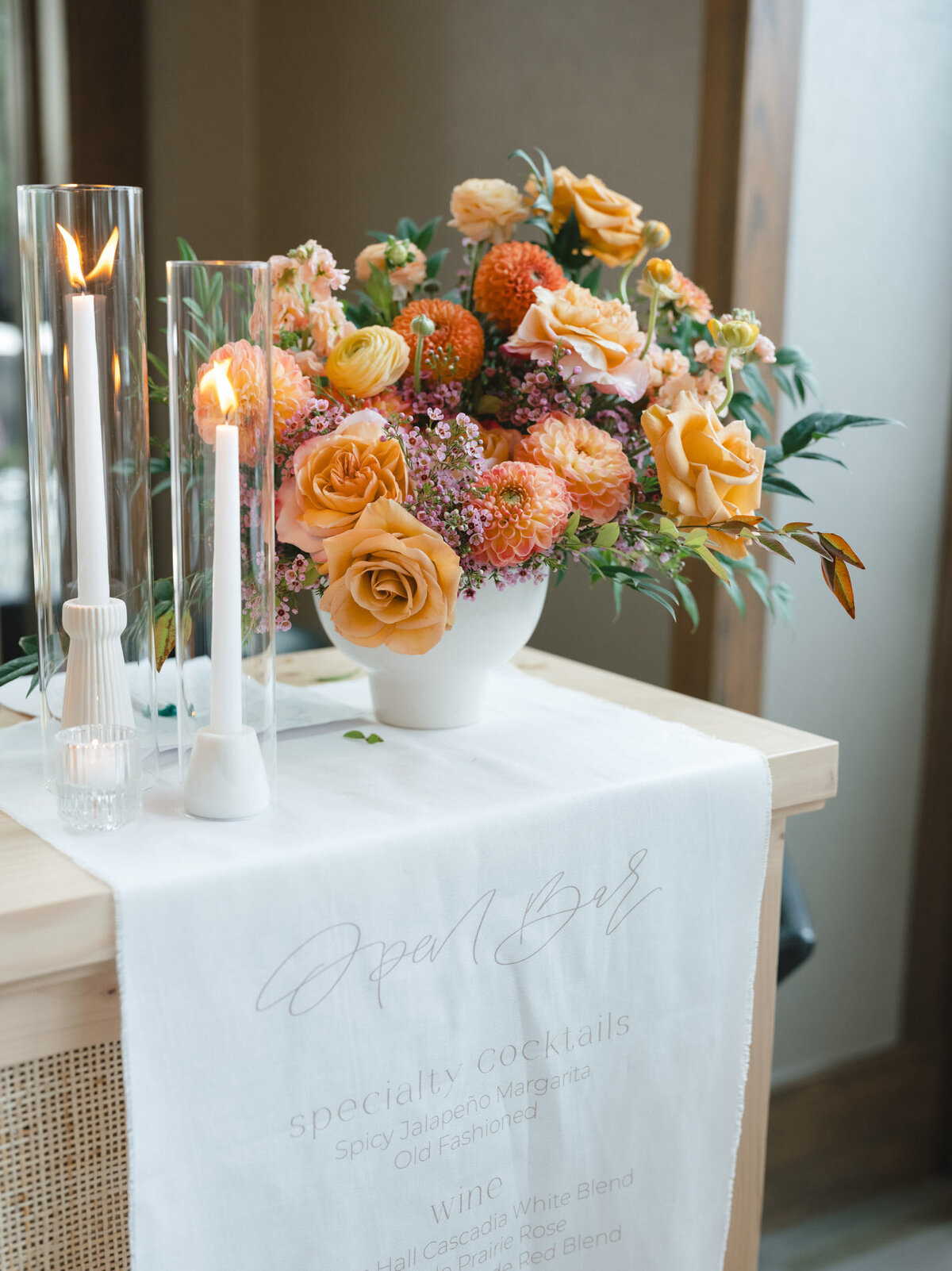 custom calligraphy bar menu on linen hanging from a rattan tabletop with florals representing full service design and calligraphy by Life in Letters.