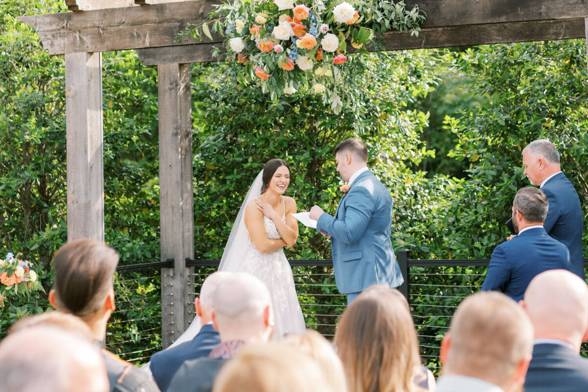 Bride smiling while groom reading his vows