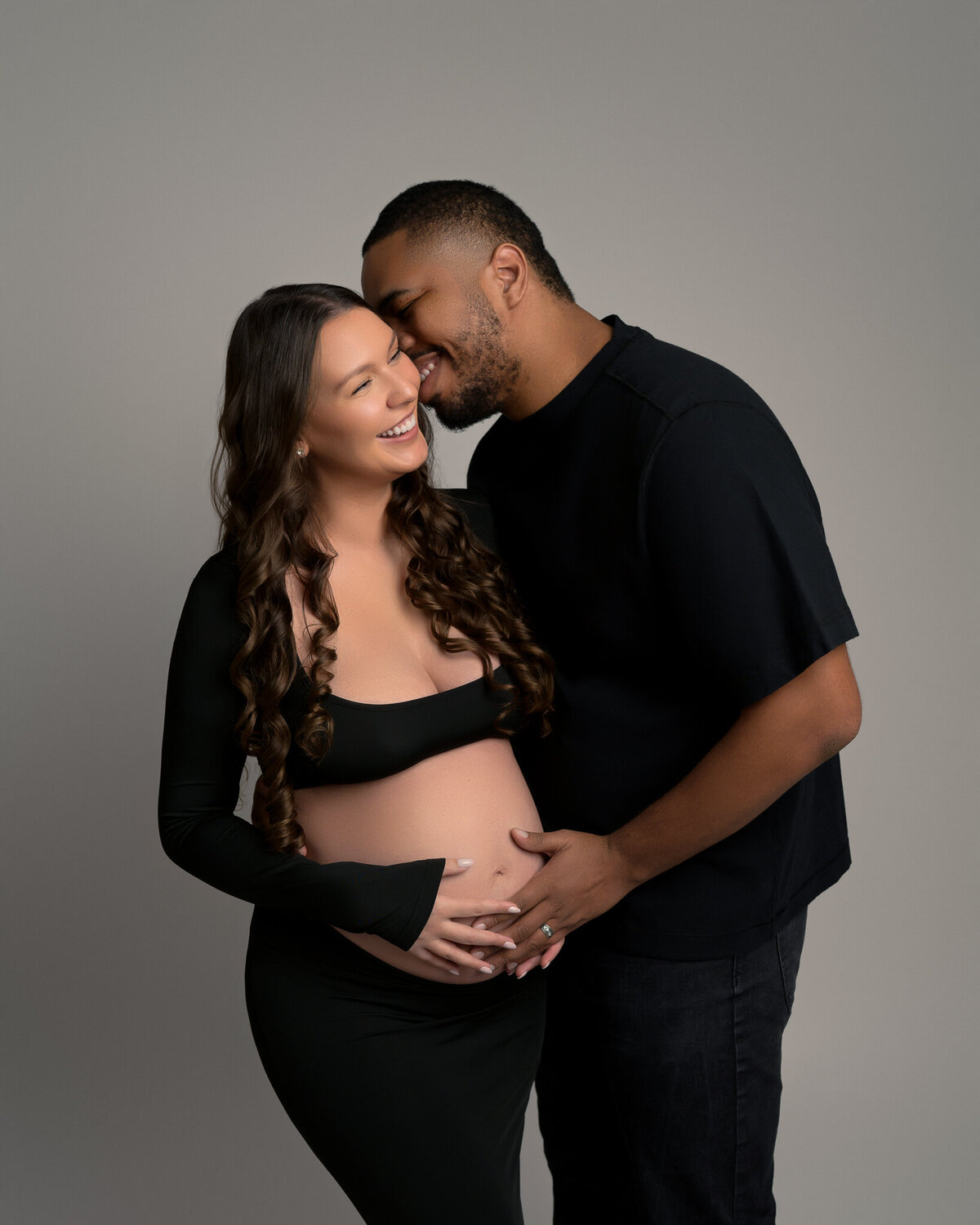 Smiling couple during studio maternity session with black gown near Cedar Park, TX