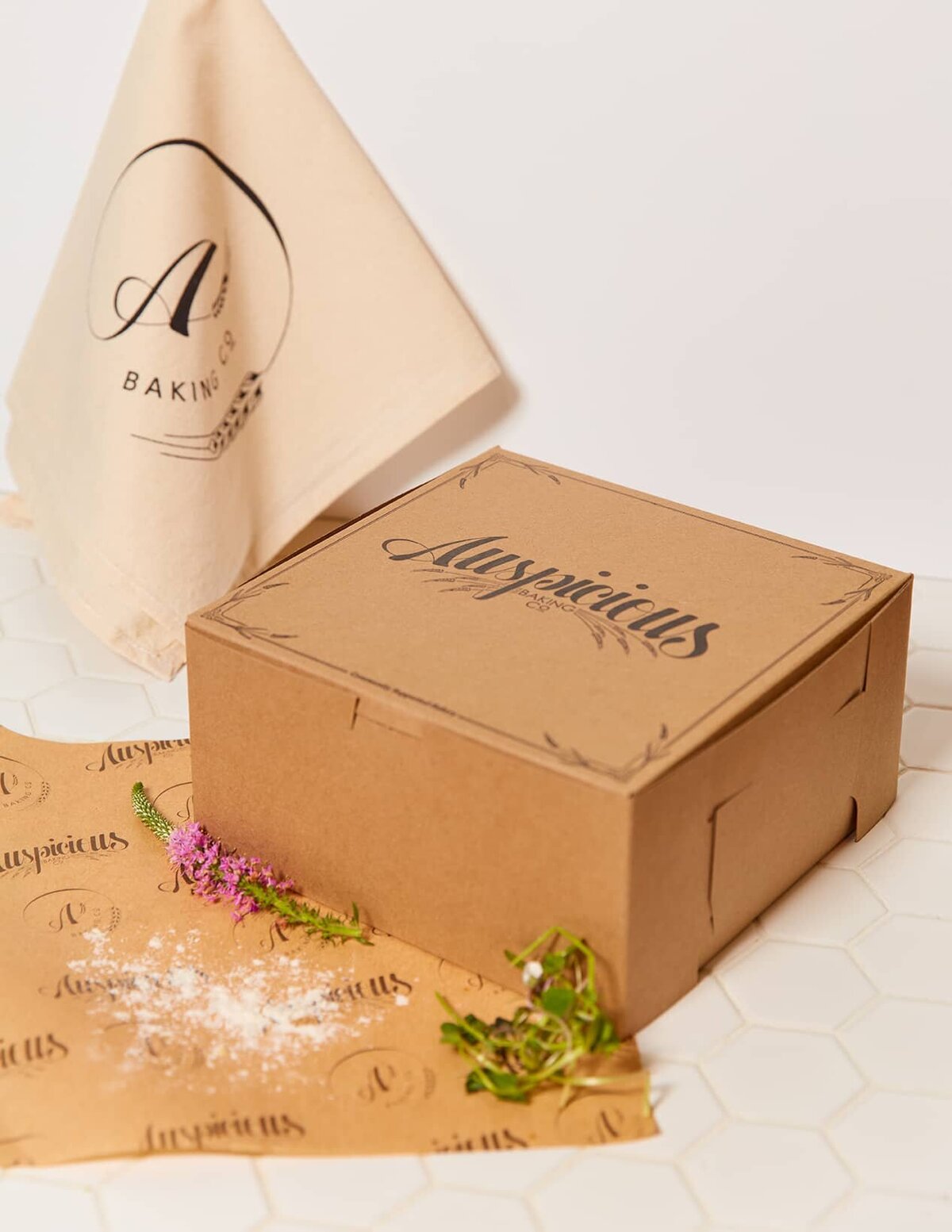 A medium-sized, brown, kraft bakery box with the Auspicious logo and custom design printed on the top