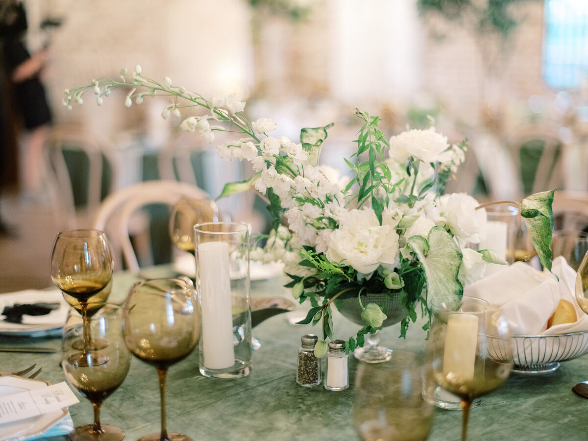 A stunning arrangement of white flowers and greenery proudly featured as a centerpiece on an elegantly set wedding dining table, enhancing the romantic evening ambiance.