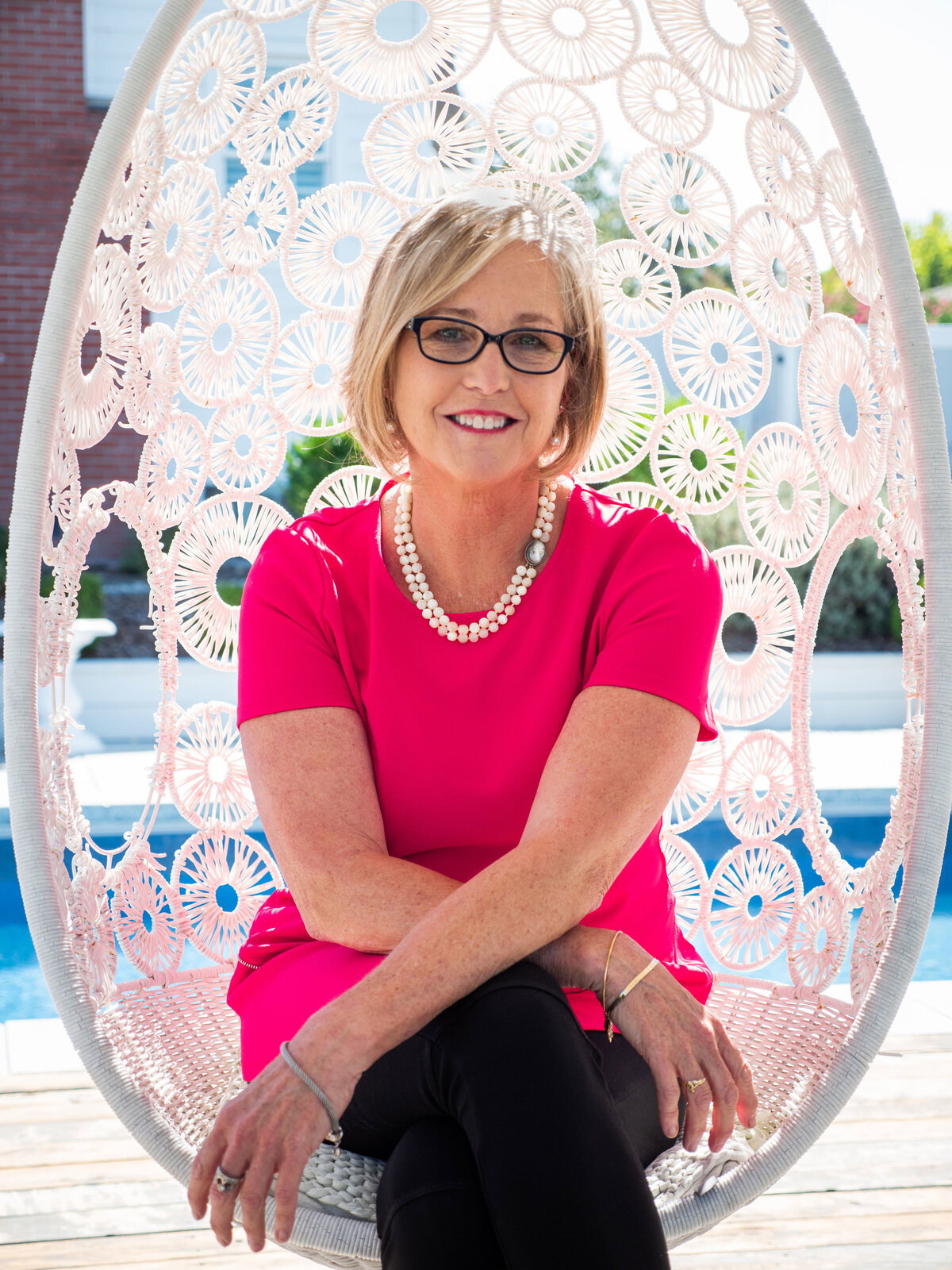 Neutral makeup for glasses paired with a pink lip to match a bright pink top sitting on a swing