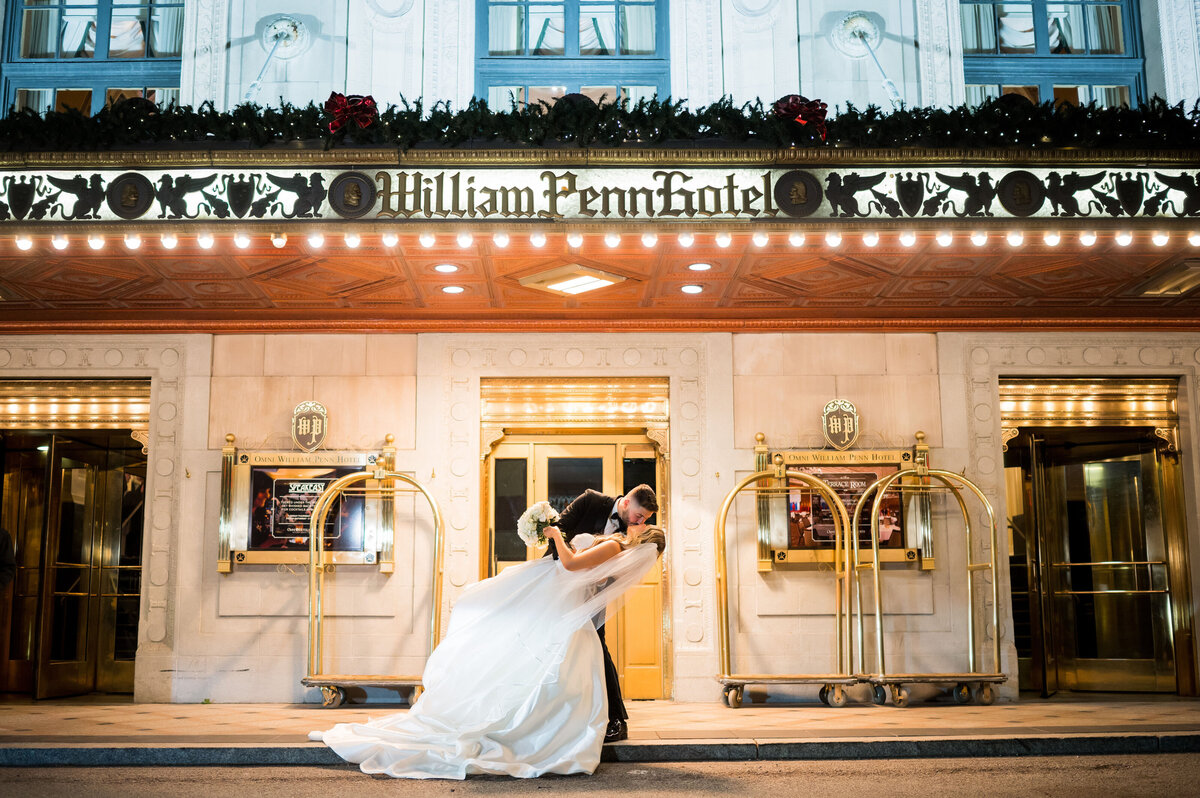 couple kissing and dipping on wedding day in front of marquee at omni william penn hotel pittsburgh
