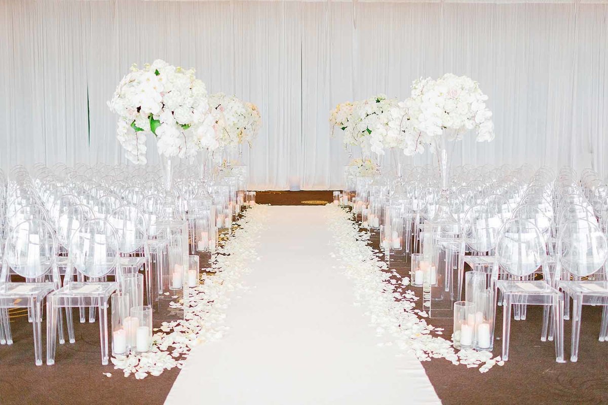 wedding ceremony aisle at Four Seasons Seattle with large white centerpieces, clear lucite chairs, and hurricane candles