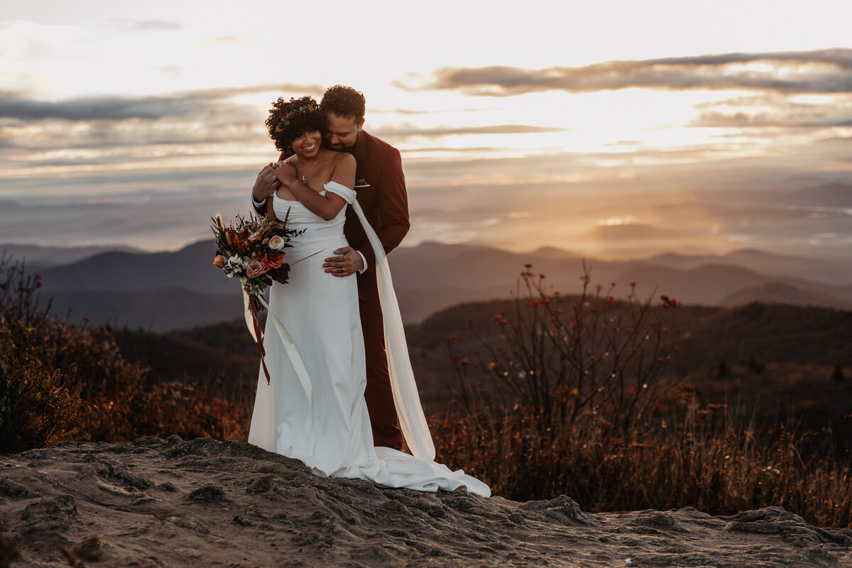 Wedding couple standing on a mountain top at sunrise at their adventure elopement in North Carolina