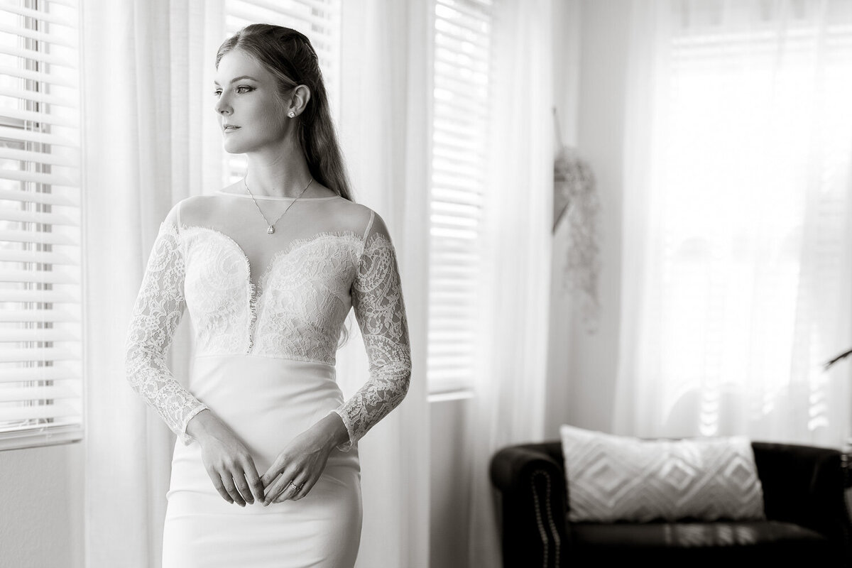 A bride gazes out a bright window in a home setting, bathed in soft natural light, during a bridal portrait session with Art of You Boudoir.