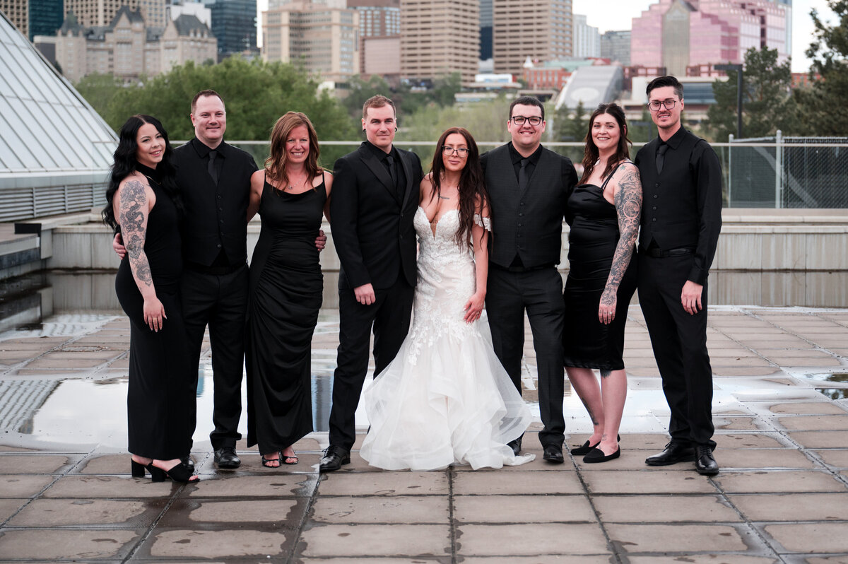 wedding party dressed in black with bride and groom standing on patio with view of downtown Edmonton in the background