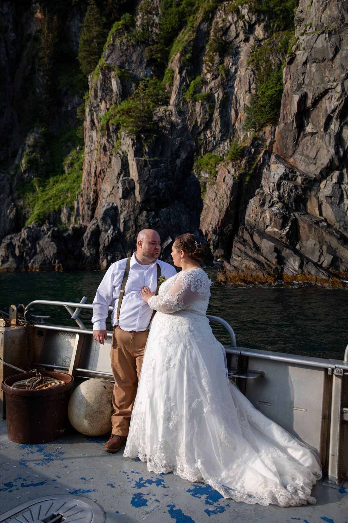 A bride and groom stand on the front of a boat on their elopement day in Alaska.