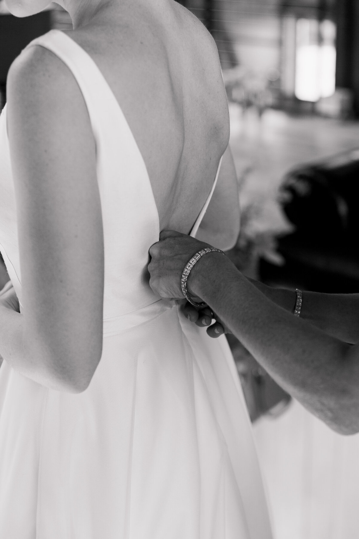 Black and white photo of someone zipping up bride's wedding dress
